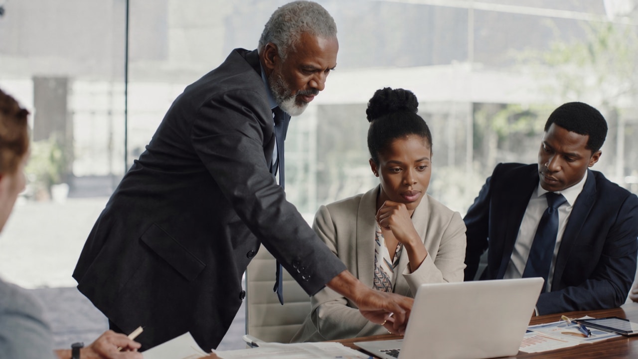 Advisors and clients reviewing strategy together around a laptop in a modern office.